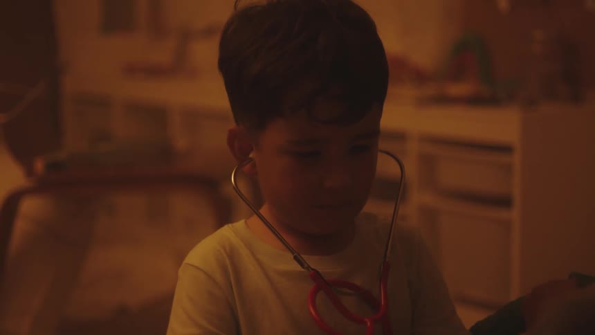 Boy playing with medical equipment to listen to the heart of another boy who is lying in bed
