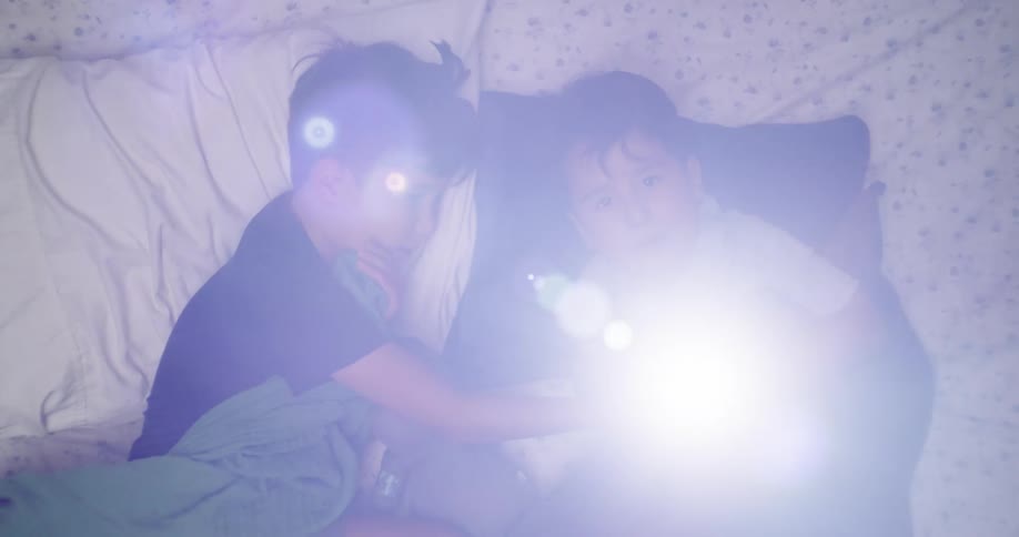 Two little boys lying down playing with a flashlight