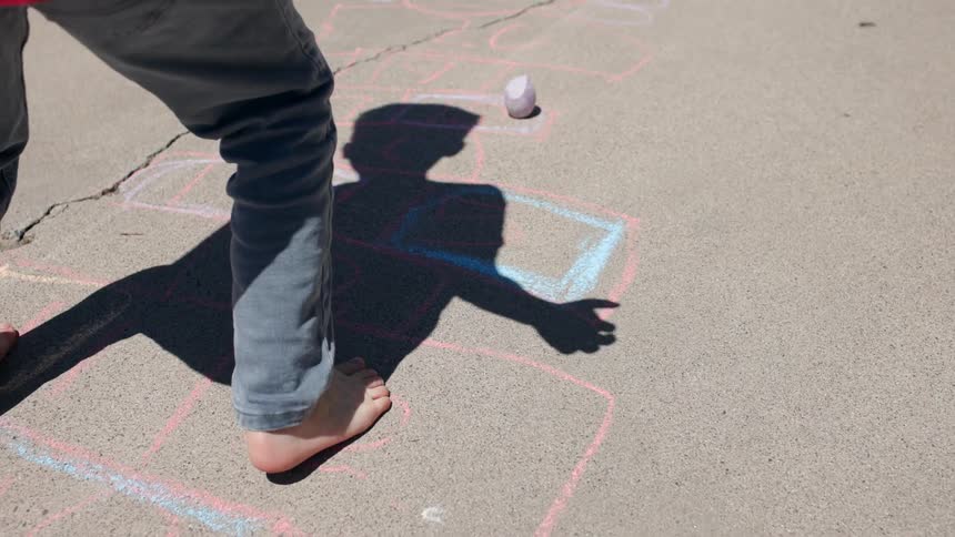 A child plays hopscotch barefoot in the street