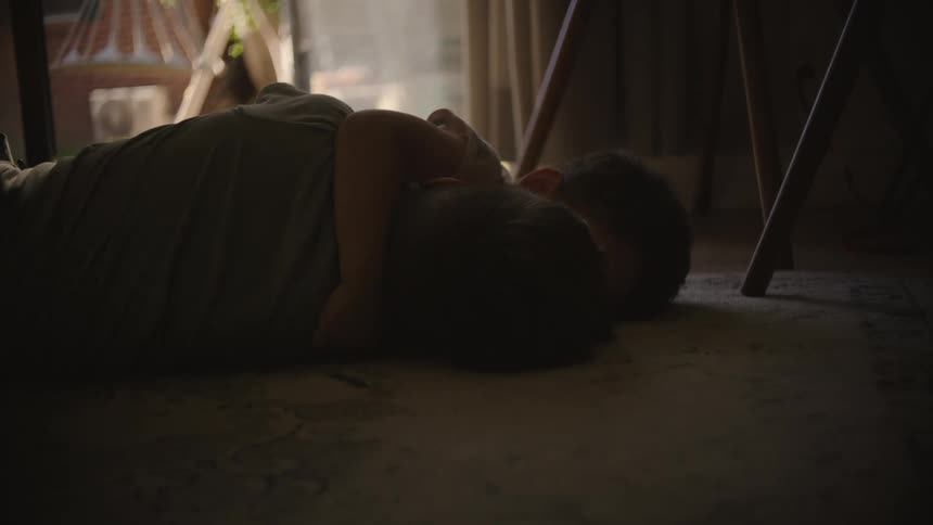 Two children lying on a carpeted floor hugging with one caressing the head of the other