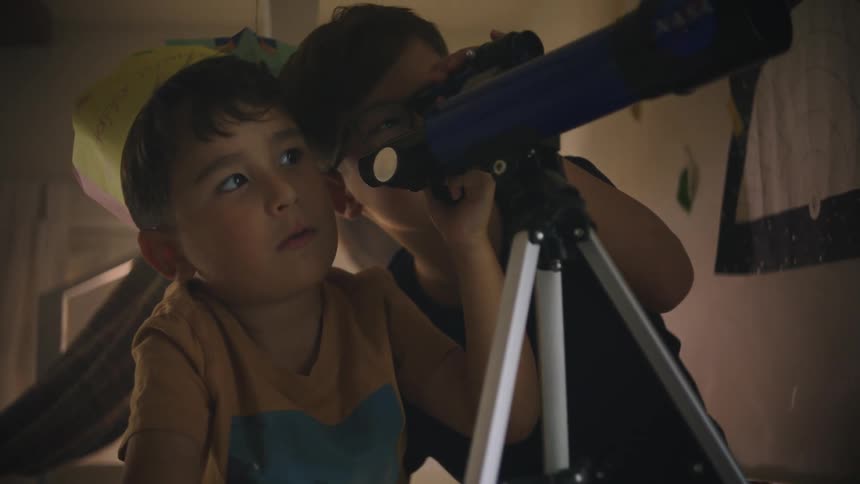 Two little boys playing with a telescope in their bedroom