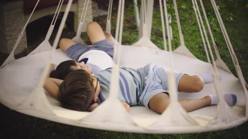 Two brothers smile as they lie on a circular swing spinning them around over a yard
