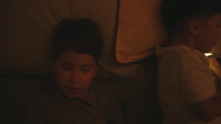 Two boys tumble into bed with one of them holding a lit flashlight