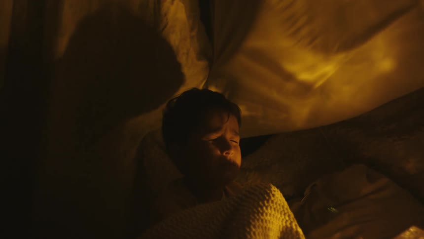 Boy wrapped in a blanket sitting with eyes closed and sheets moving around