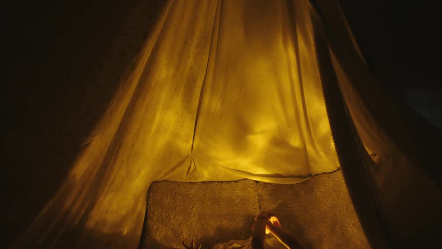Two boys make shadow puppets on the side of a tent