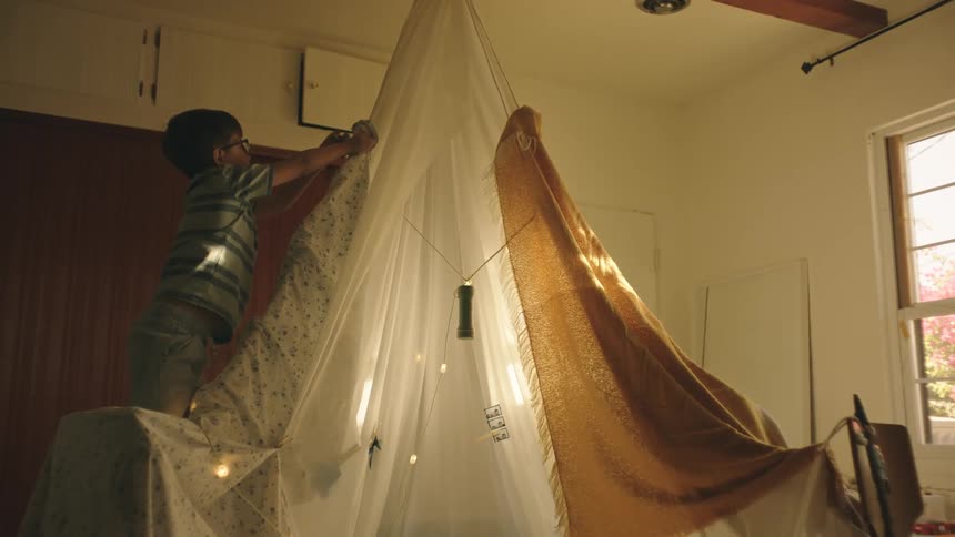 A young boy helps build an indoor tent made out of sheets and curtains