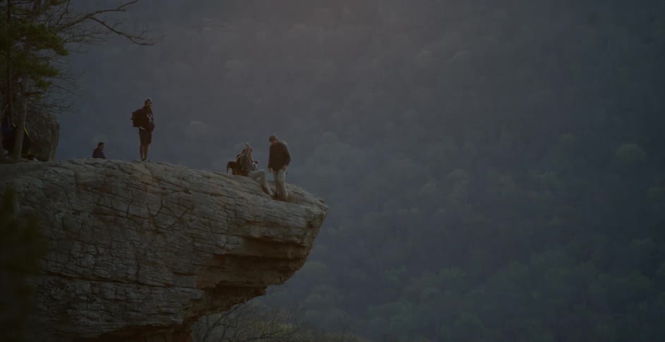A man helps a woman to a seat on the edge of a cliff outcropping