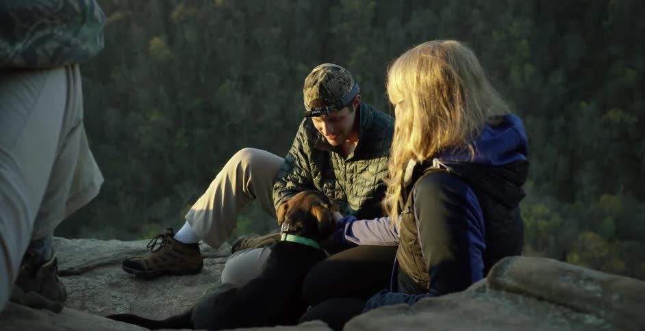 People sitting outside in the mountains and petting a dog