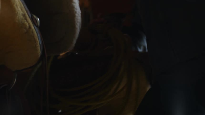 Blonde woman picks upa saddle and other horse tack