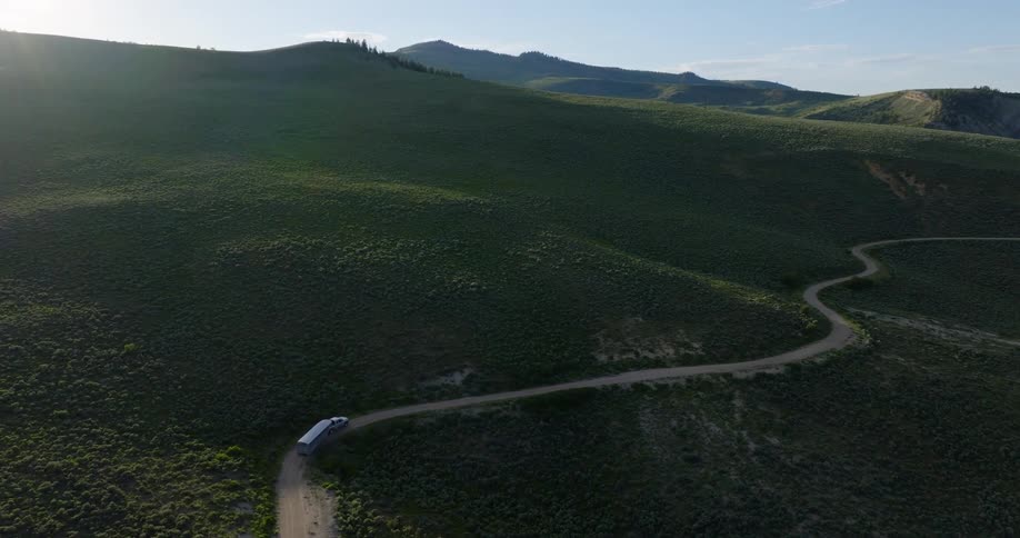 A truck hauling an animal trailer drives around hills on a winding road
