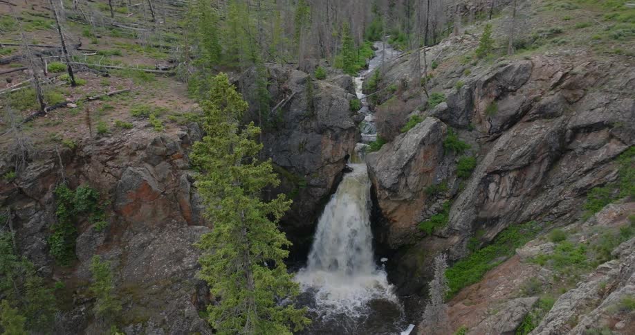 A waterfall cascading down a rocky cliff into a pool below surrounded by pine trees and rugged terrain