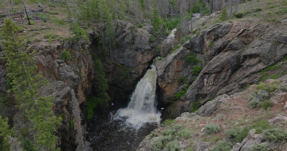 A river turns into a mountain waterfall close to a sparse forest