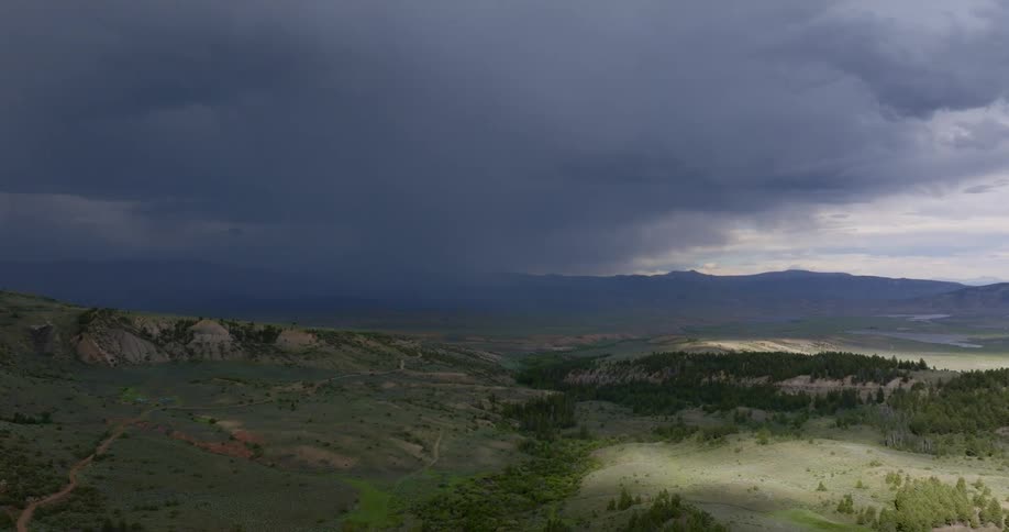 Dark clouds drop rain over a plain and a mountain range