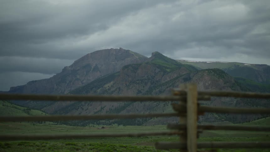 Dark clouds hover over a mountain range visible from a farm