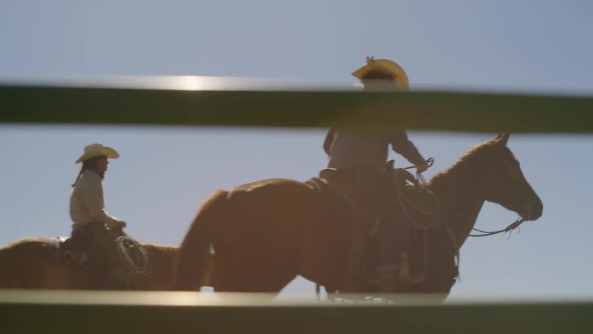 Four cowboys rides horses inside of a closed farm area