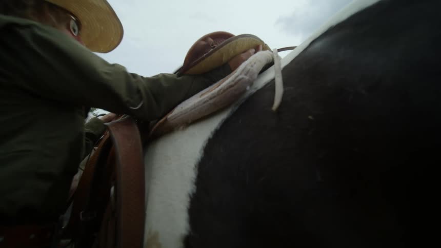 Woman placing a seat on top of a horse