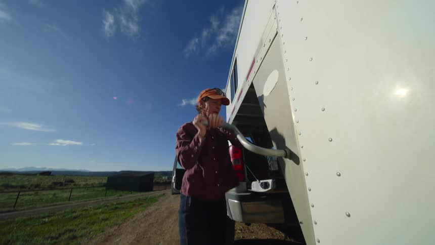A woman rotates a handle that is on the side of her livestock trailer