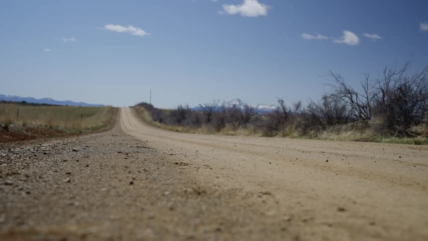 A dirt road runs between stunted bushes and open fields