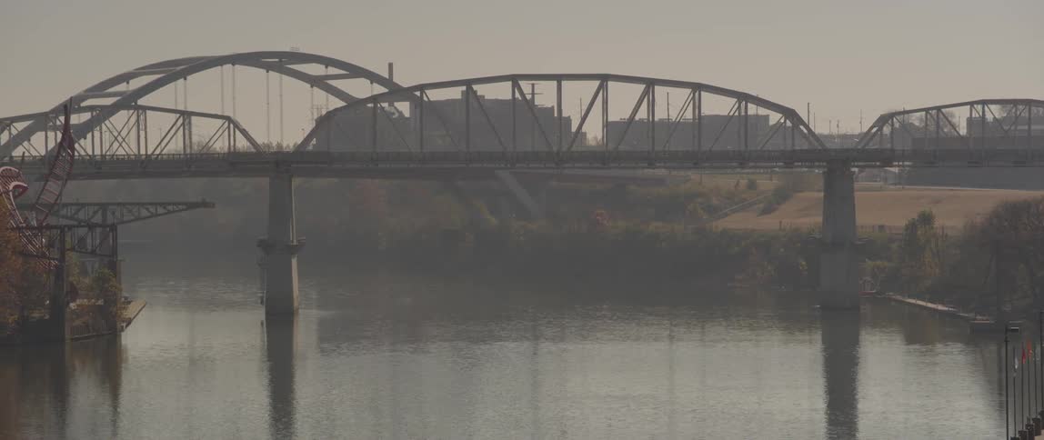 A view of a bridge spanning a river with some industrial buildings in the background