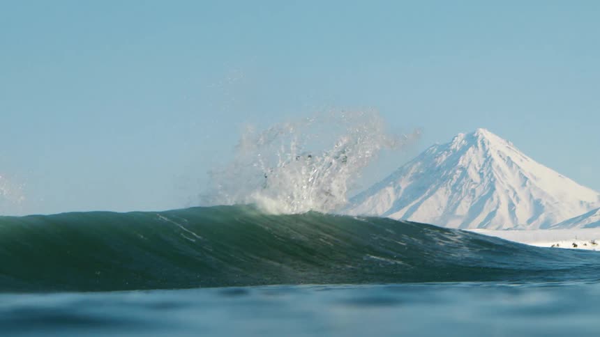 Person doing a trick at the peak of a wave and snowy mountains on the horizon