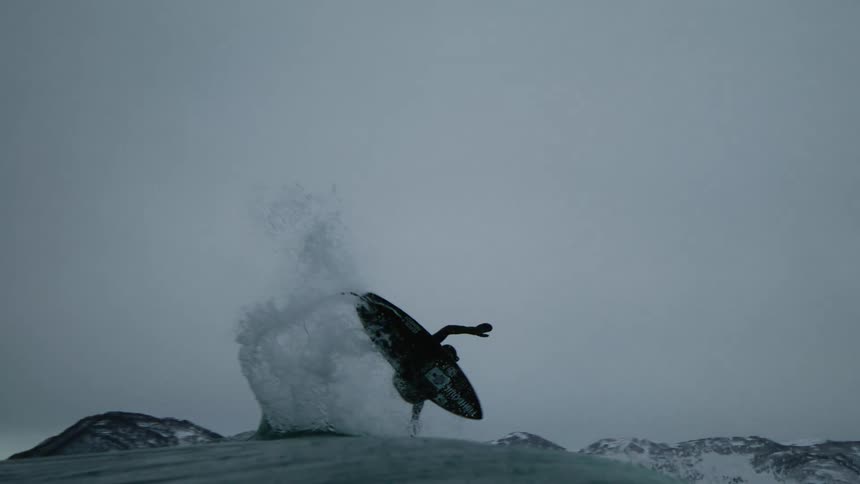Person with a surfboard doing a maneuver and staying suspended in the air on a wave in the ocean