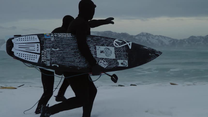 Two surfers with their surfboards walking in the snow towards the beach