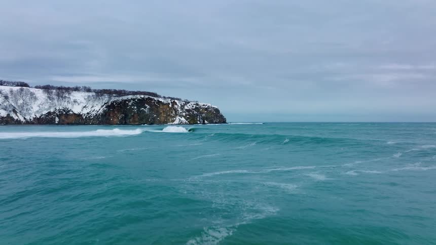 Waves roll to shore near cliffs partially covered in snow