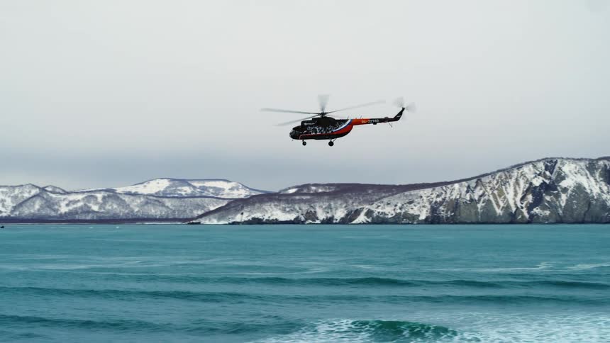 Helicopter flying above the sea with snowy mountains in the background