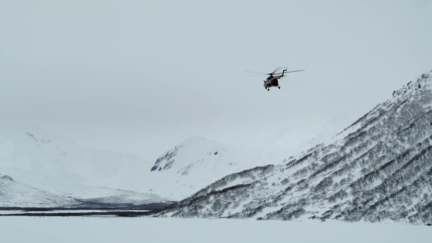 Helicopter flying above snow covered mountains