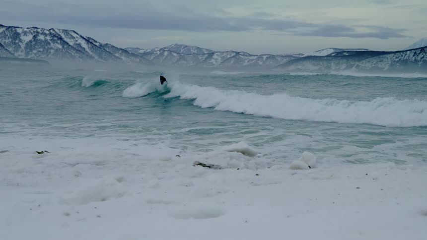 Surfer doing a radical maneuver on the wave with snowy mountains in the background