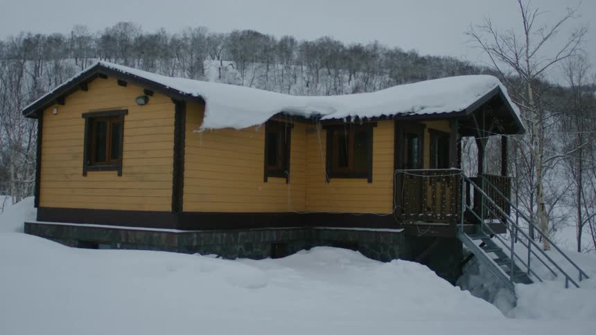 Light snow falling on a yellow cabin surrounded by snow in the mounains