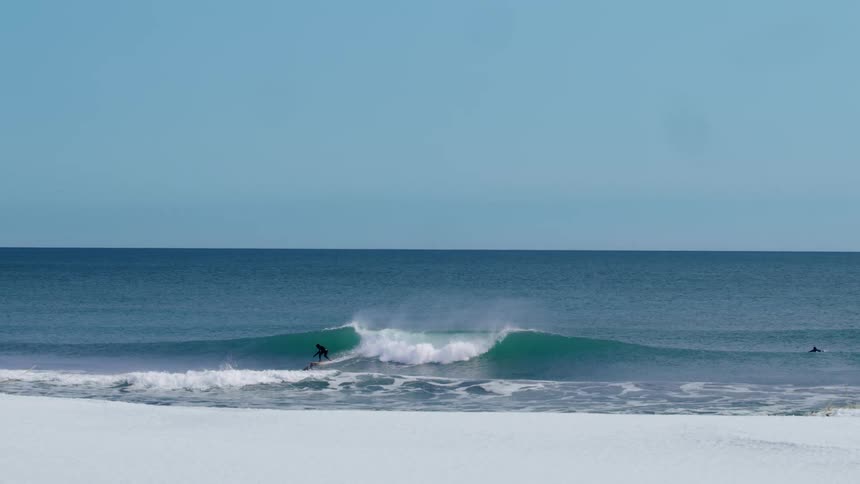 Person dropping and surfing a wave during a cloudless blue sky day