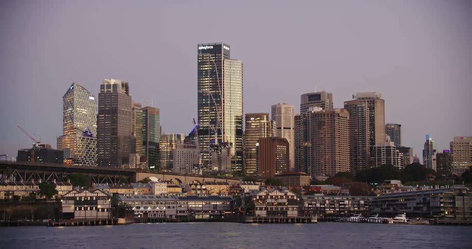A busy port area sits right off the water near a railway bridge and skyscrapers in a downtown city area