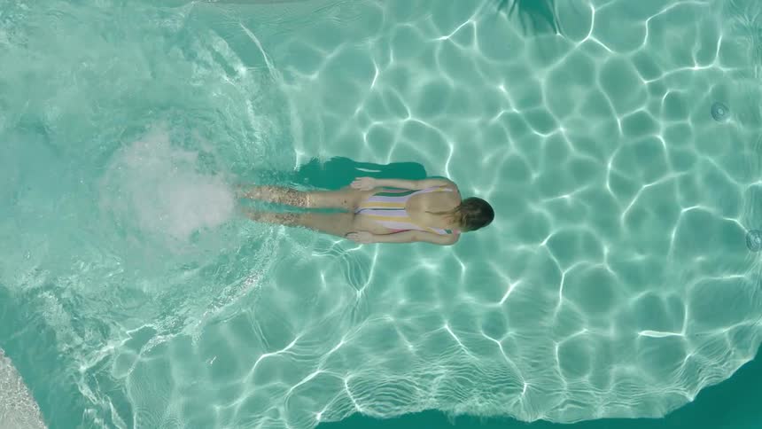 Overhead view of a woman swimming underwater in a turqouise swimming pool
