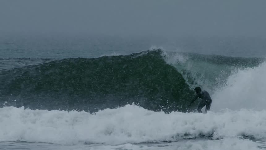 Surfer dropping into a strong wave and doing maneuvers on a rainy day