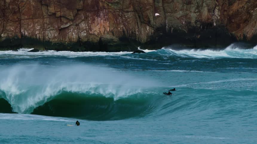 Surfers surfing in a rough ocean with the rocky coastline in the background