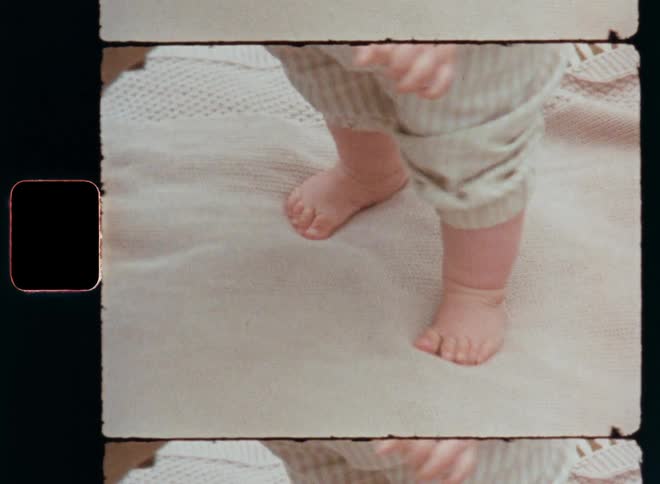 Hands of an adult holding or helping a baby to walk while it is moving the legs with bare feet up and down and dancing on the spot with positive energy and excitement having fun and enjoying learning new things on 8mm retro film