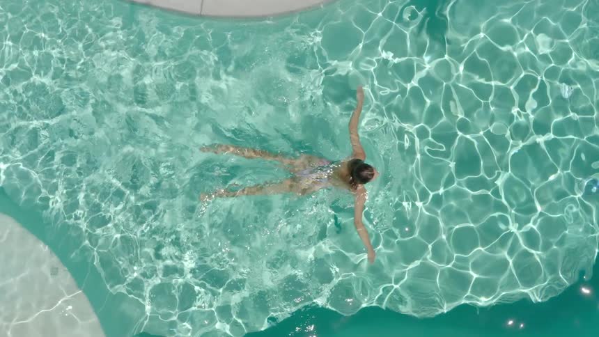 Top view of a blue pool with sun reflection and a woman swimming