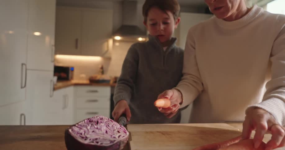 Mother teaching her son how to cut carrots in the kitchen