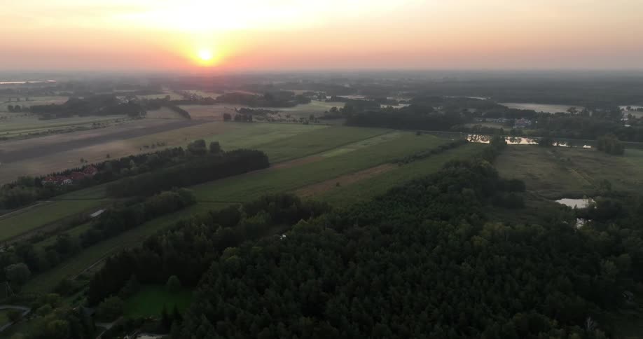 The sun shines low on the horizon over a rural area with forests and farm fields
