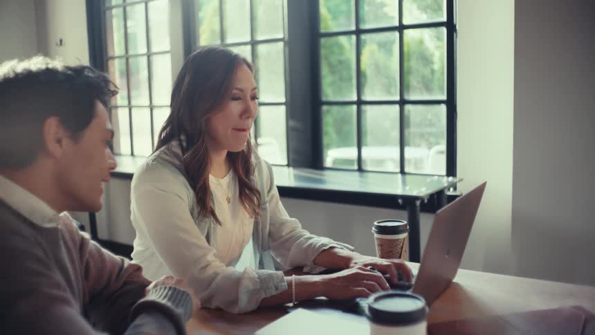 Two people working together on a desk near large windows
