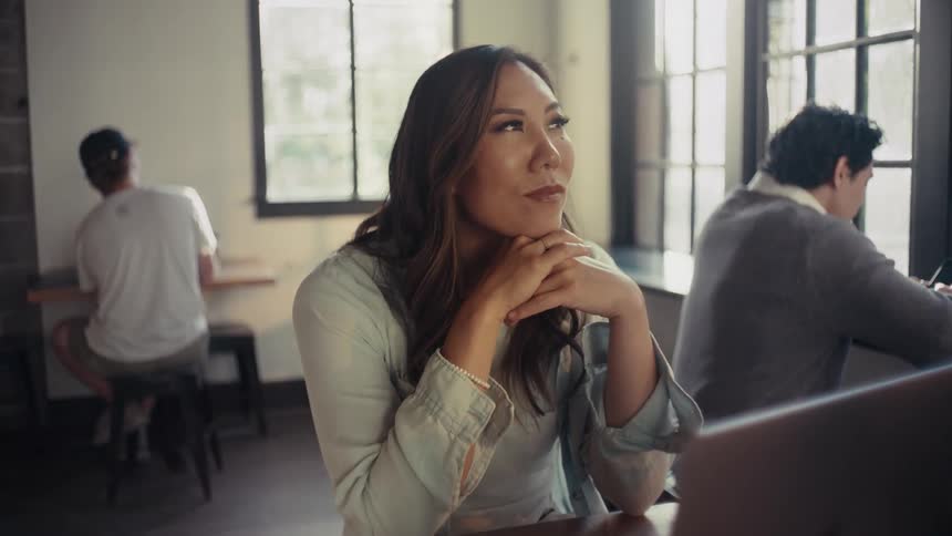 Woman sitting at an office desk thoughtfully with a happy facial expression