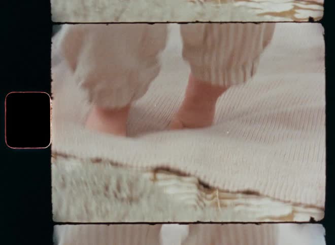 Close up of the feet and legs of an unrecognisable happy baby being held by a parent and jumping on the spot before it starts walking with shaky legs while learning how to walk and taking the first steps as childhood milestone on vintage 8mm