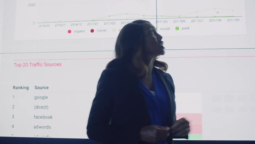 Woman in a dark room presenting a slide on a large screen with graphs