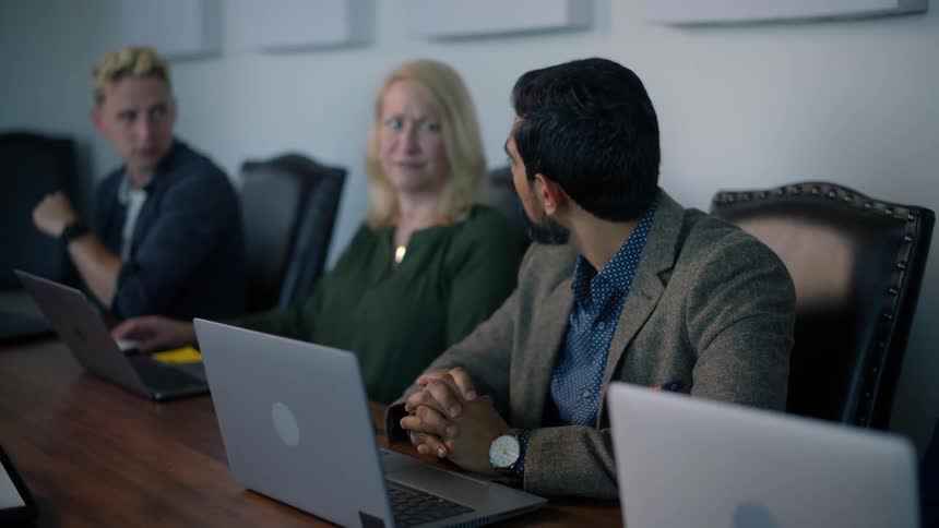 Group of people sitting at a table with laptop talking to each other