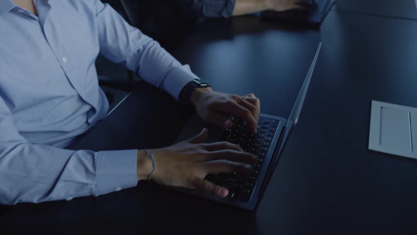 The hands of several people in an office typing on laptops that are on a table