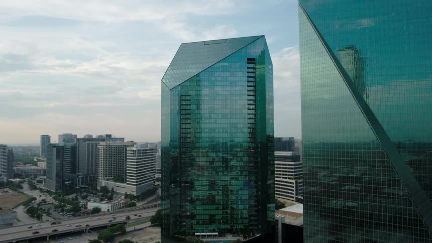 Two large buildings with their external architecture composed of glass that are reflecting the other buildings in the city