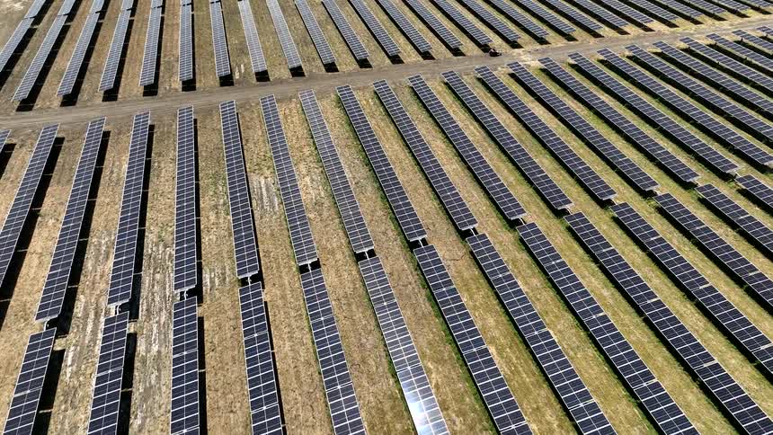 A large farm of solar panels pointing upwards with some dirt roads between them
