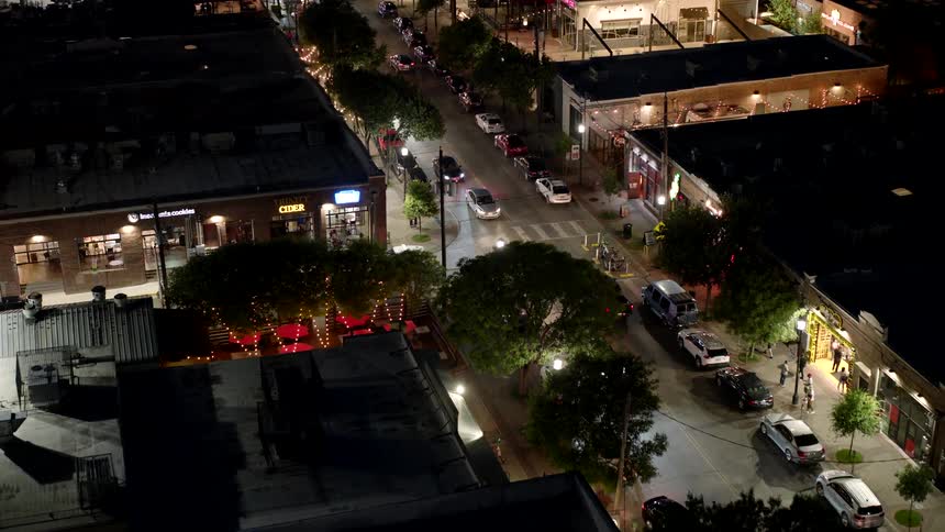 An aerial night view of a busy street with illuminated buildings and vehicles