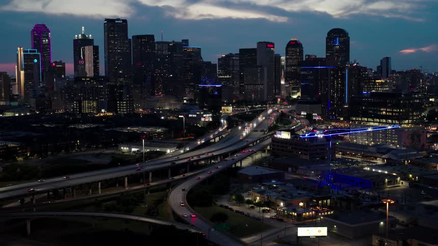 Aerial view of a highway with intersections and traffic and skyscrapers in the background in a metropolis at the beginning of the evening